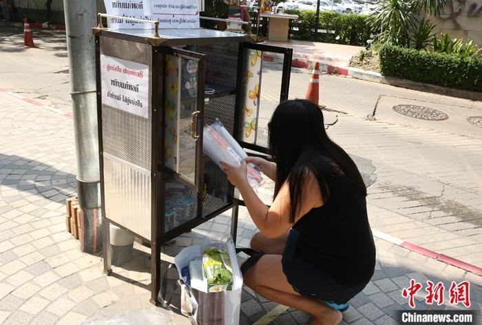 5月14日，一名善心人士在泰国曼谷一住宅小区路口给“共享食物柜”添加物品。/p中新社记者 王国安 摄